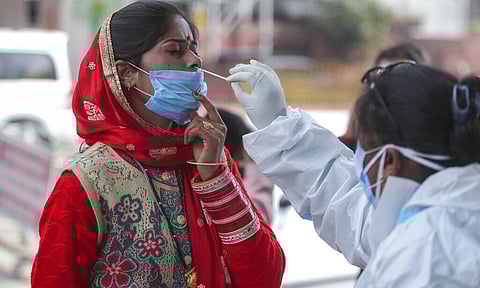 A health worker collects a swab sample from a woman to test for COVID-19 by a road side in Jammu, India. (Photo | AP)