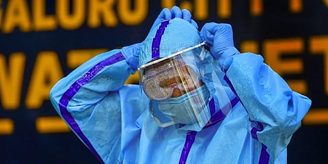 A health worker adjusts his face shield as he prepares to collect swab samples of passengers for the COVID-19 test at KSRTC bus stand in Bengaluru. (File Photo | PTI)