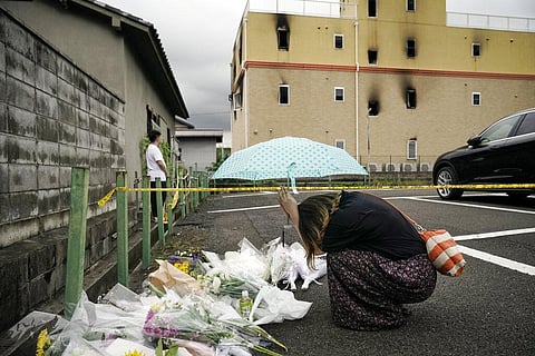 a woman prays at a makeshift memorial to honor the victims of a fire at the building of Kyoto Animation's No. 1 studio, background, in Kyoto, western Japan.