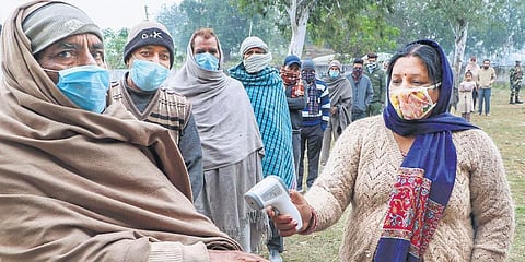 Voters undergo thermal screening as they wait to cast their votes in the DDC polls at Suchetgarh village, about 25 km from Jammu, on Wednesday. (Photo | PTI)