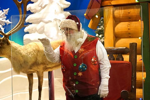 Santa Claus waves at children and their families from behind a transparent barrier at a shop in Miami. (Photo | AP)