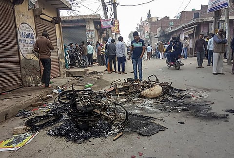Passersby look at the charred remains of vehicles which were set ablaze by rioters during clashes over the new citizenship law at Mustafabad area of East Delhi Tuesday Feb. 25 2020. (Photo | PTI)