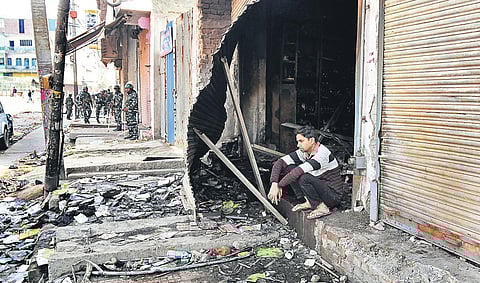 Security forces are seen in a riot-hit street in northeast Delhi as a youth sits outside a gutted shop. (Photo | Parveen Negi, EPS)
