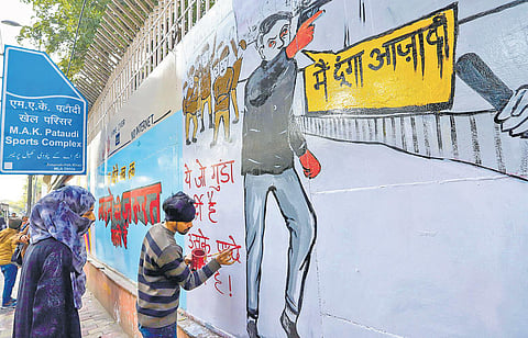 An activist paints graffiti on a wall to protest against the recent incidents of firing at Jamia Millia Islamia & Shaheen Bagh. (Photo | PTI)