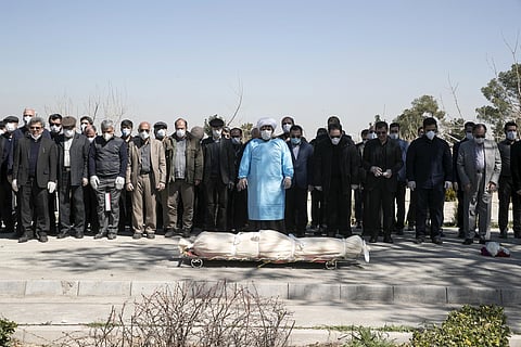Mourners wearing face masks and gloves pray over the body of former politburo official in the Revolutionary Guard Farzad Tazari, who died Monday after being infected with the new coronavirus, at the Behesht-e-Zahra cemetery just outside Tehran, Iran, Tues
