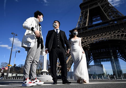 Vietnamese tourists wearing face masks and wedding clothes stand in front of the Eiffel tower in Paris. (Photo | AFP)
