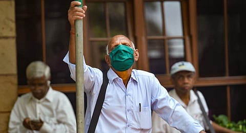 A man wears a mask as a preventive measure against coronavirus and watches stock prices on a screen on the BSE building, in Mumbai. (Photo | PTI)