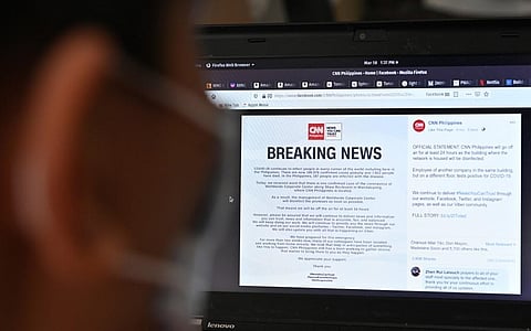 A man reads an announcement by CNN Philippines of their temporary closure from their facebook page, due to a positive COVID-19 infection at their building in Manila on March 18, 2020. (Photo | AFP)