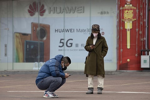 Residents wearing masks look at their smartphones near an advertisement for 5G smartphones from Chinese tech giant Huawei in Beijing. (Photo | AP)