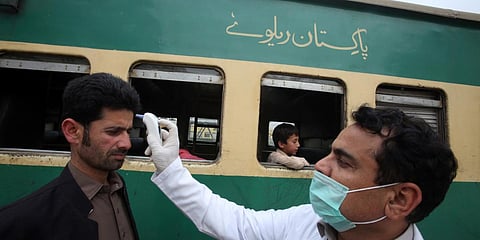 A Pakistani volunteer checks the body temperature of passengers arriving at a railway station in Peshawar. (Photo| AP)