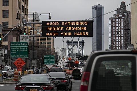 The Manhattan bridge is seen in the background of a flashing sign urging commuters to avoid gatherings, reduce crowding and to wash hands in the Brooklyn borough of New York. (Photo | AP)