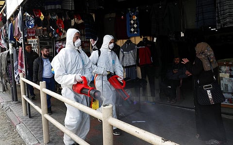 Workers wearing protective gear spray disinfectant as a precaution against the coronavirus, in front of shops at the main market in Gaza City. (Photo | AP)