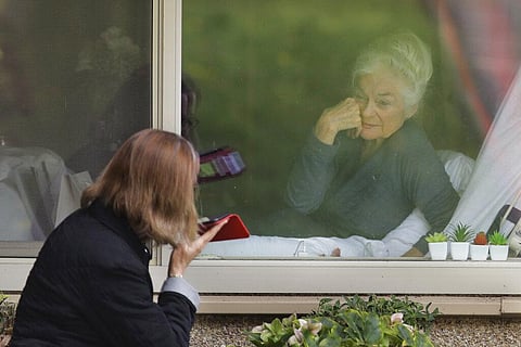 A coronavirus positive patient smiles as she visits through the window and on the phone with her daughter at the Life Care Center in Kirkland, near Seattle. (Photo | AP)