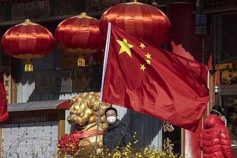 A masked man looks out near a national flag outside a traditional medicine hospital in Beijing. (Photo | AP)