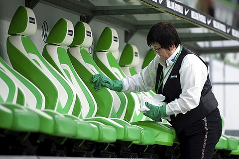 A woman desinfects the seats of the substitute bench prior to the German Bundesliga match in Wolfsburg. (Photo | AP)