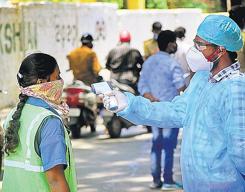 A pourakarmika gets her temperature checked by a health worker in Padarayanapura in Bengaluru on Sunday | pandarinath b