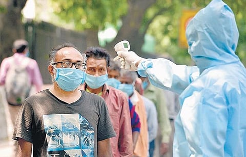 A man wearing protective suit checks the temperature of people outside Indian Youth Congress headquarters in New Delhi | pti