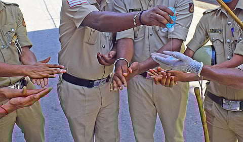 Bengaluru City Police personnel share a bottle of hand sanitiser in Padarayanapura, Chamarajpet, on Monday I Pandarinath B