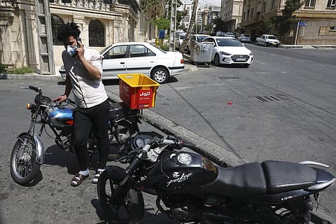 Grocery deliveryman Saeed Vatanparast, wears a protective face mask to help prevent the spread of the coronavirus, speaks on his cellphone outside a store in Tehran. (File photo | AP)
