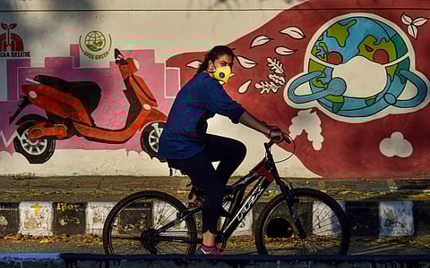 A woman cycles past a wall graffiti during the COVID-19 lockdown in New Delhi, Sunday, April 26, 2020. (Photo | PTI)