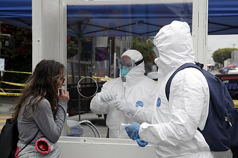 In this April 20, 2020, file photo, members of the Los Angele Fire Department wear protective equipment as they conduct a new coronavirus test on a woman, left, in the Skid Row district in Los Angeles. (Photo | AP)
