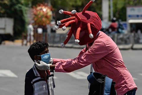 A man wearing a coronavirus-shaped mask helps a small boy wear a safety mask. (Photo | EPS)