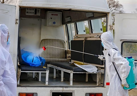 A municipal worker wearing protective suit sprays disinfectant solution on the body of a person who died of COVID-19 before its burial during the nationwide lockdown in Ahmedabad Thursday April 30 2020. (Photo | PTI)