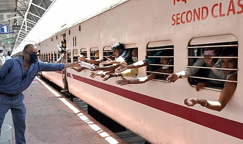 A railway employee provides water bottles to migrants sitting in a train to reach their native places during the ongoing COVID-19 lockdown in Jabalpur. (Photo | PTI)