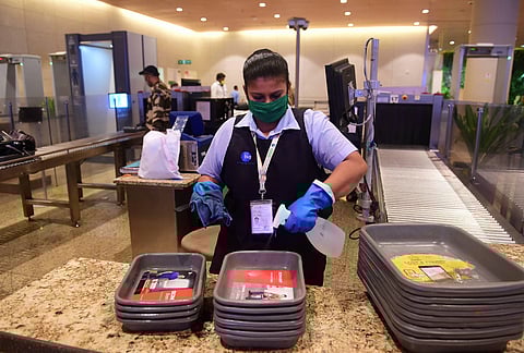 An airport official sanitizes trays at the security check area of the Chatrapati Shivaji Maharaj International airport during a media tour to witness the preparedness post resuming operations in Mumbai Thursday May 28 2020. (Photo | PTI)