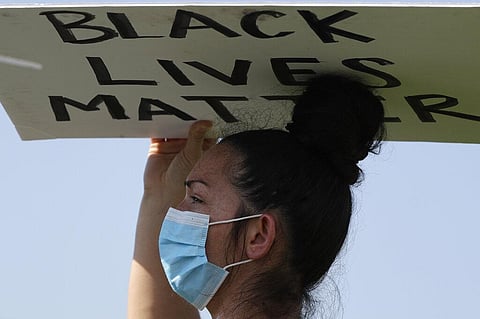 A demonstrator holds a sign for George Floyd during a Black Lives Matter protest in Buffalo Grove. (Photo | AP)