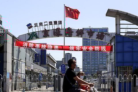 A man and a child wearing protective face masks to help curb the spread of the new coronavirus ride on an electric-powered scooter passes by the seafood wholesale market which was closed for inspection in Beijing, Sunday, June 14, 2020. (Photo | AP)