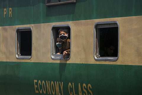 Boys wearing protective masks to help curb the spread of the coronavirus, look out the window of a train at a railway station, in Karachi, Pakistan. (File Photo | AP)
