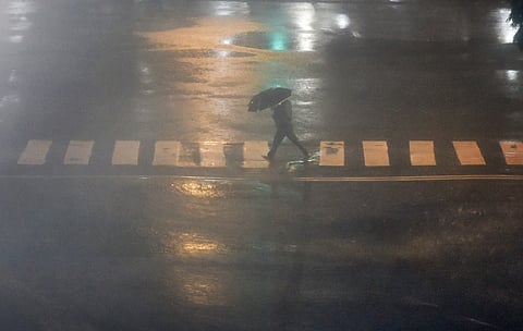 A pedestrian takes cover under an umbrella during heavy monsoon rain. (File | PTI)