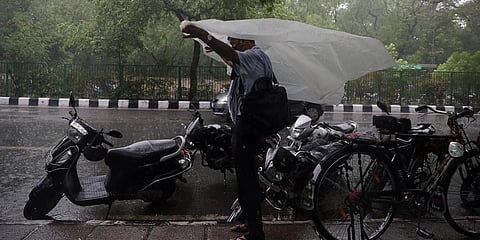 A man protects himself with a plastic sheet during a rainfall, in New Delhi. (Photo| ANI)