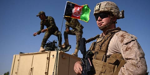 A US Marine looks on as Afghan National Army soldiers raise the Afghan National flag on an armed vehicle during a training exercise. (File photo| AFP)