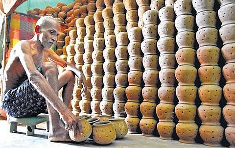 Nagalla Balaramaiah sits in a shed, next to stacks of traditional clay pots.