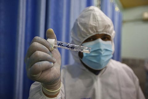 A health official in protective gear holds sample collected from a man at a screening and testing facility for COVID-19. (Photo | AP)