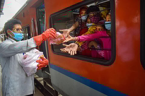 A railway staff member distributes food packets among migrants sitting in Shramik Special train to reach their native places during ongoing COVID-19 lockdown at Prayagraj Railway Station Sunday May 31 2020. (Photo | PTI)