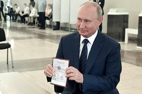 Russian President Vladimir Putin shows his passport to a member of an election commission as he arrives to take part in voting at a polling station in Moscow on Wednesday. (Photo | AP)