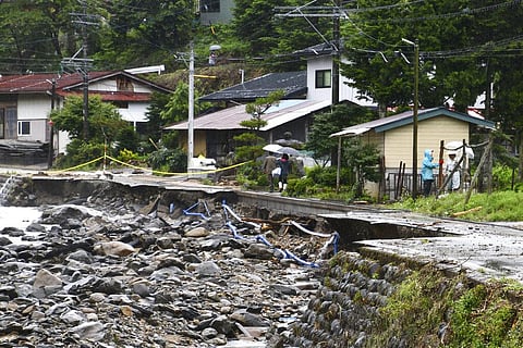 People walk on a road damaged by water following a heavy rain in Takayama, Gifu prefecture, central Japan Friday, July 10, 2020. Parts of Nagano and Gifu, including areas known for scenic mountain trails and hot springs, have been flooded by massive downp