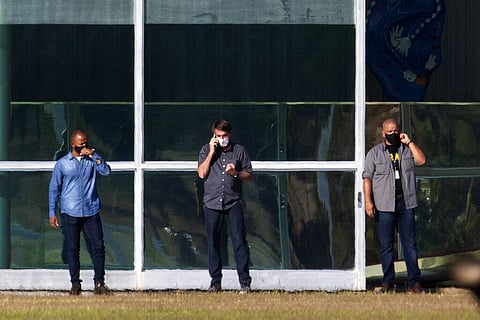 Brazil's President Jair Bolsonaro, center, talks on his phone while standing outside his official residence Alvorada Palace, in Brasilia, Brazil, Friday, July 10, 2020. (Photo | AP)