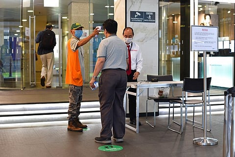 A man wearing a face mask uses a thermal scanner to check on the temperature of an individual before he can enter a building in Singapore. (File photo | AP)