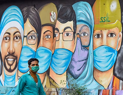 A man walks past a graffiti honouring COVID-19 warriors (Photo| PTI)