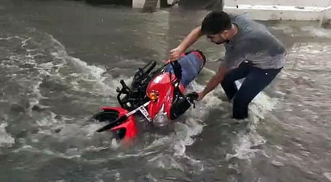 A man trying to save two-wheeler as heavy rainfall triggered flash floods in parts of Sehore. (File photo| ANI)
