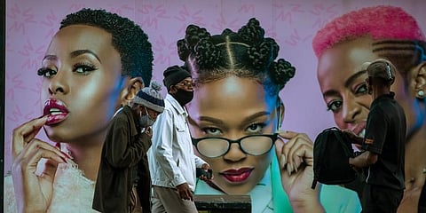 Men wearing face masks to protect against coronavirus, walk past an advertising billboard on the street in Soweto, South Africa. (Photo | AP)