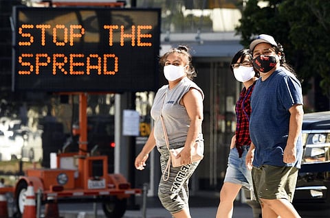 Pedestrians wear masks as they walk in front of a sign reminding the public to take steps to stop the spread of coronavirus. (Photo | AP)