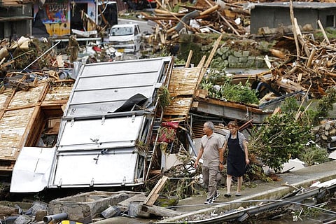 A couple walks near debris from a heavy rain in Kumamura, Kumamoto prefecture, southern Japan Monday, July 6, 2020.
