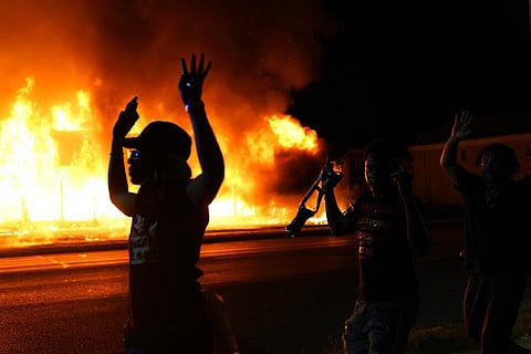 Protesters walk past police with their arms up, late Monday, Aug. 24, 2020, in Kenosha, Wis., as a building burns in the background. (Photo | AP)