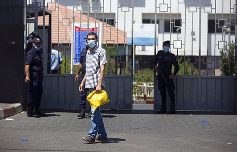 A Palestinian man wears a face mask as he walks next to Hamas police officers guarding the entrance of the Shifa Hospital where coronavirus cases were discovered, in Gaza City. (Photo | AP)