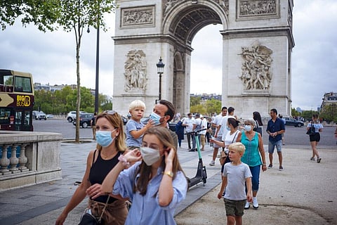 A family wearing protective face masks walk along on the Champs Elysee avenue, with Arc de Triomphe in background, in Paris. (Photo | AP)